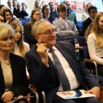 Ludzie siedzący na widowni podczas wydarzenia, skupieni i uśmiechnięci.