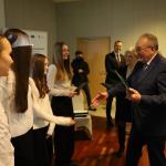 Mężczyzna wręcza dyplomy grupie uśmiechniętych dziewcząt w białych koszulach.