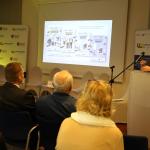 Kobieta prowadzi prezentację przed publicznością, slajd wyświetlany na ekranie.