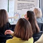 Kobiety siedzące tyłem na konferencji, słuchają prelegenta.