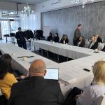 Spotkanie biznesowe przy dużym stole konferencyjnym, ludzie słuchają prezentacji.