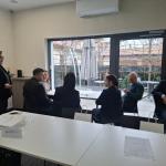 Kilka osób siedzi przy stole w sali konferencyjnej, jedna osoba stoi obok.