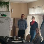 Cztery osoby podczas prezentacji w sali konferencyjnej, przy stole i tablicy z notatkami.