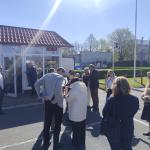 grupa ludzi stojąca przed budynkiem w słoneczny dzień