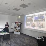 prelegent wygłaszający referat obok wyświetlanego slajdu na kolorowym tle 